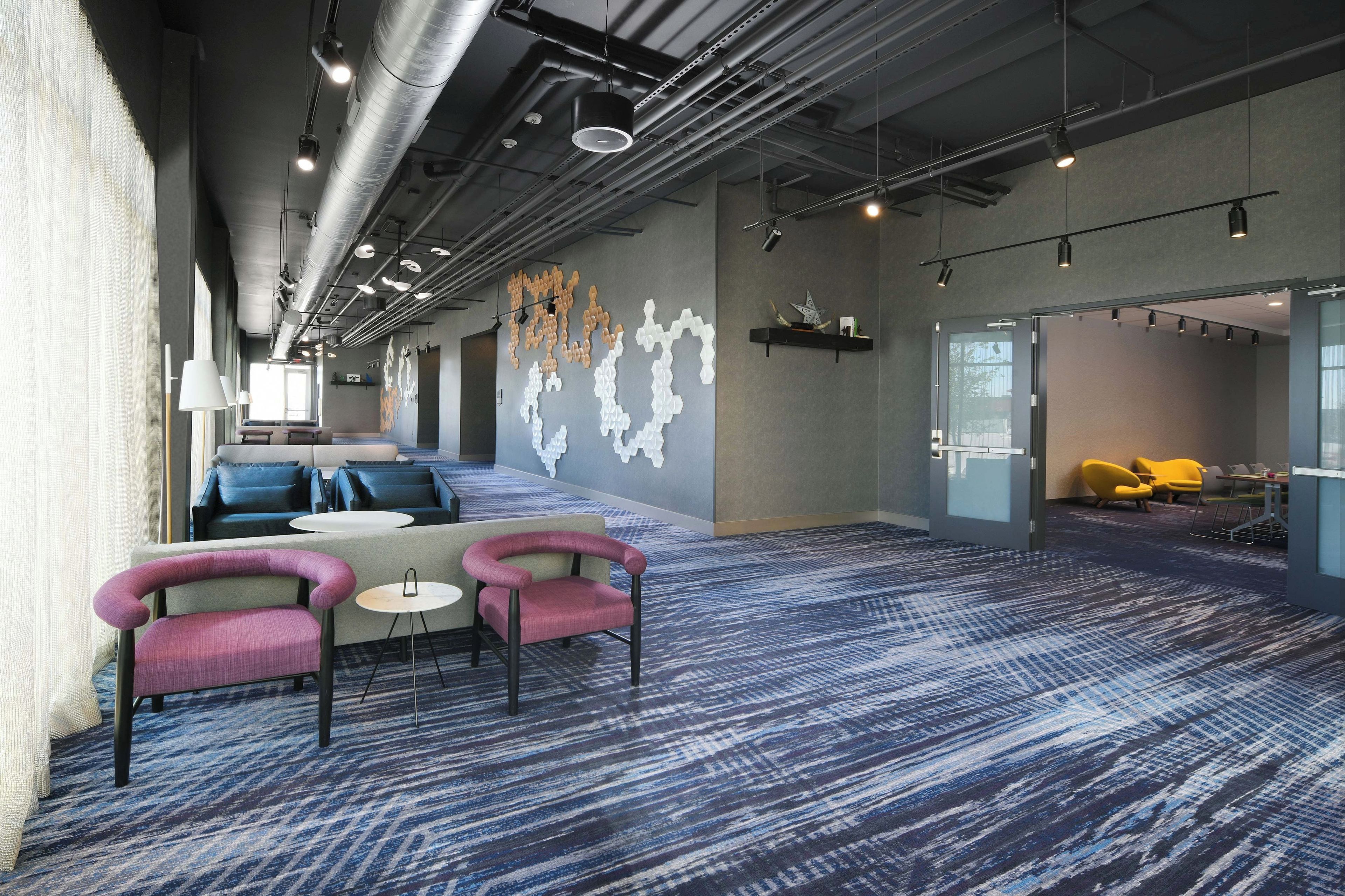 A modern lounge area with seating, a patterned carpet, and a wall with abstract art.