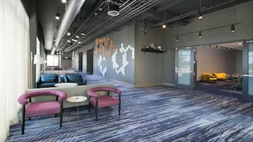 A modern lounge area with seating, a patterned carpet, and a wall with abstract art.