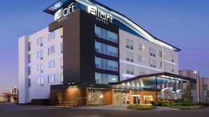 Un hotel moderno con un llamativo letrero de 'Aloft Hotel', una entrada de vidrio y una fachada bien iluminada.