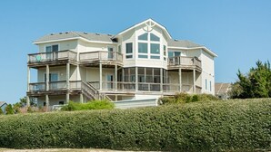 Ein großes, mehrstöckiges Haus mit einem auffälligen Balkon im zweiten Stock, einer umlaufenden Veranda und einem großen Erkerfenster im dritten Stock.