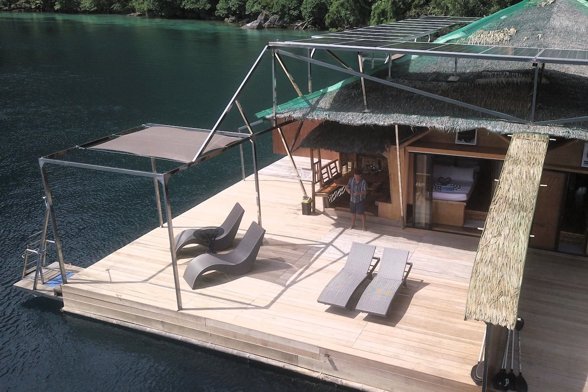 Una estructura flotante con terraza, sillas de descanso y un área cubierta con techo de paja.