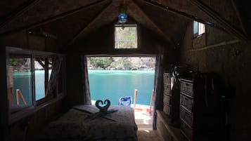 A cozy room with a bed, a small window, and a view of a body of water.
