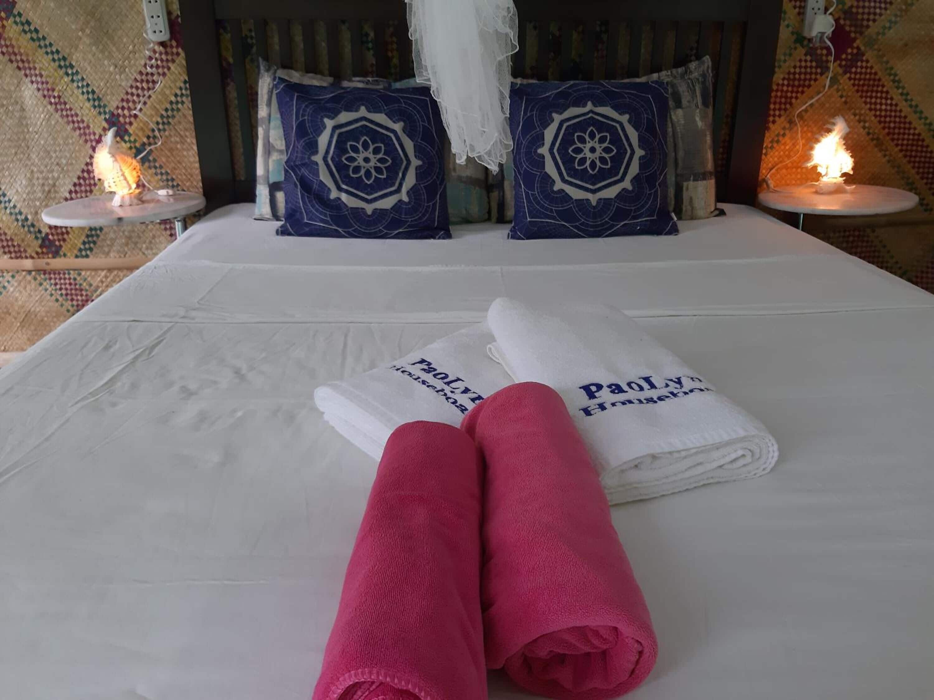A neatly made bed with two folded towels, two decorative pillows, and two bedside lamps.
