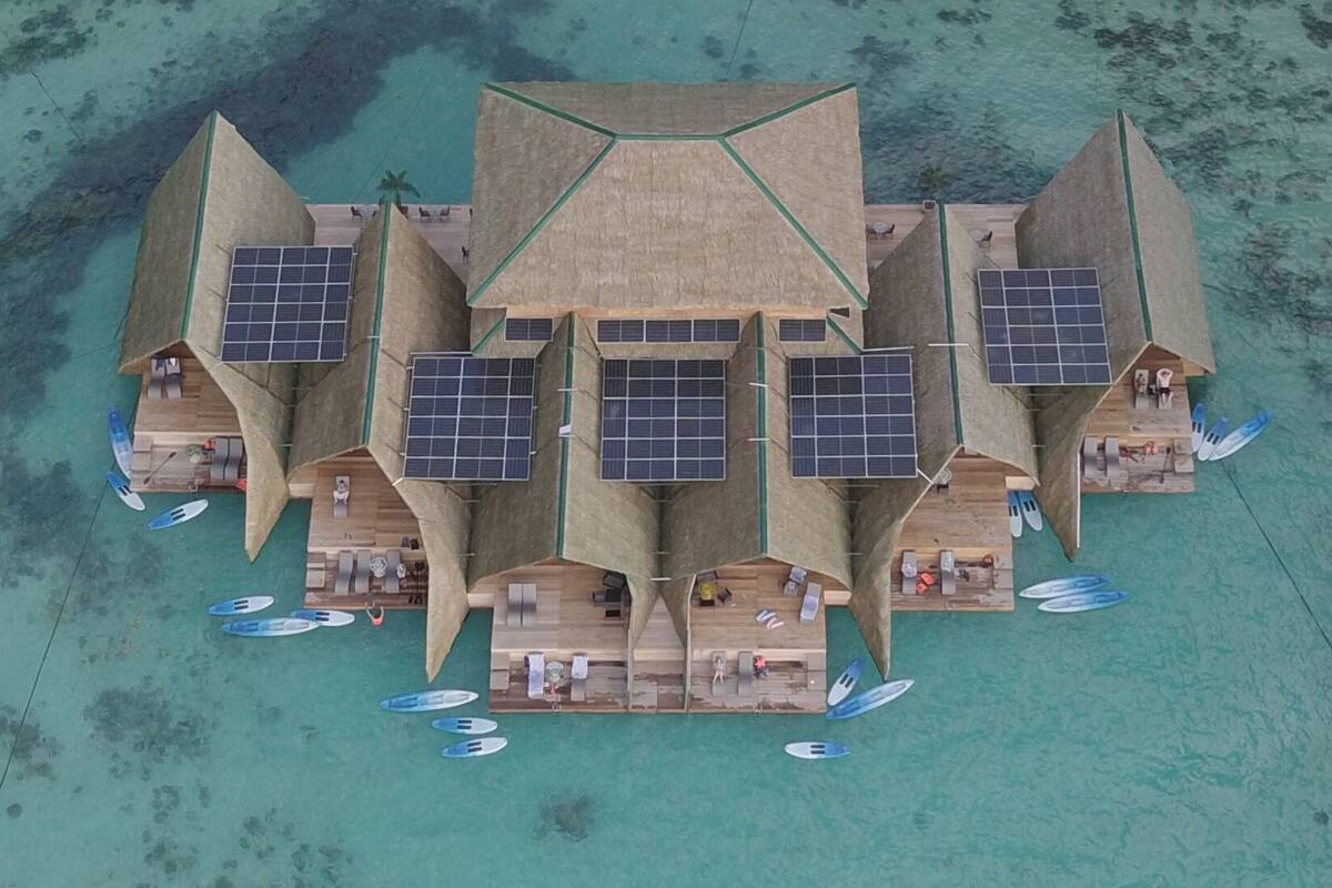 Un resort con varias villas, cada una con un panel solar en el techo, una piscina y vista a la playa.