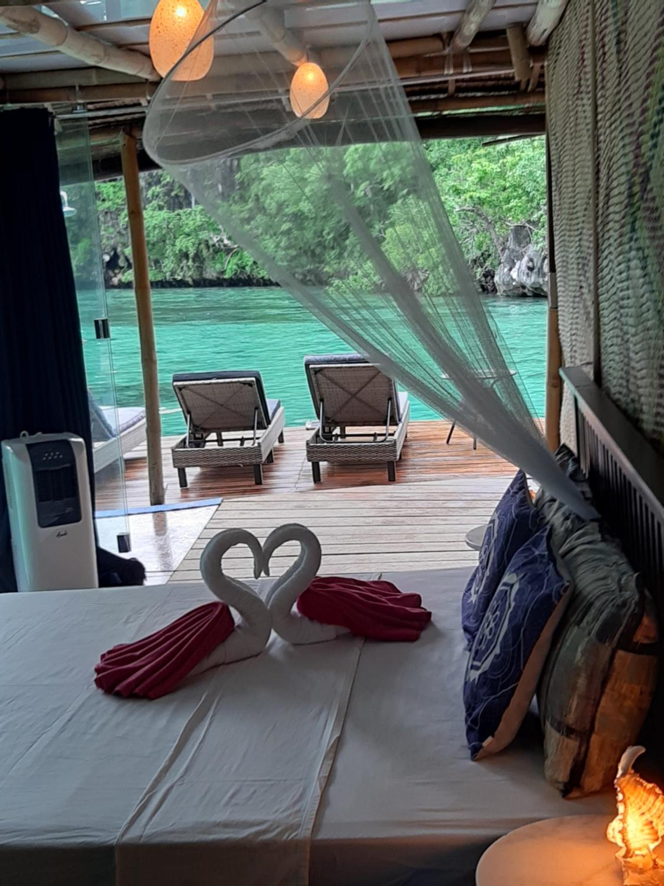 A room with a bed, two lounge chairs, a canopy, and a view of a body of water.