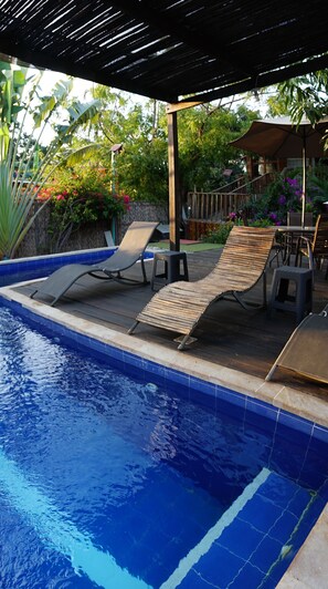 Una piscina al aire libre, sombrillas, sillones reclinables de piscina