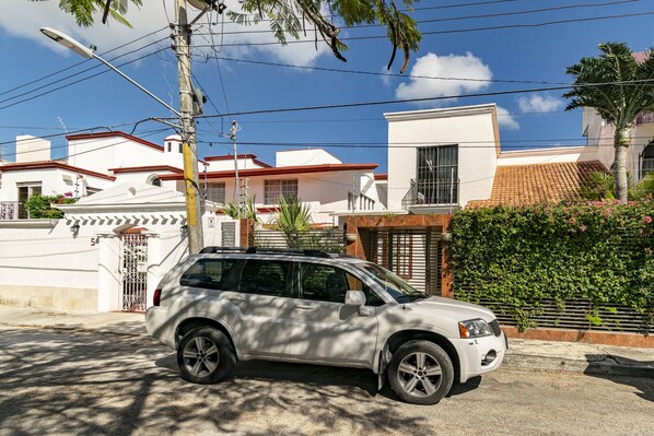 Un VUS blanc est garé dans une rue, avec un bâtiment blanc en arrière-plan.