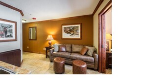 A living room with a brown leather sofa, two round wooden ottomans, a side table with a lamp, and framed artwork on the walls. - Two bedroom Two Bath with private lock-off unit (Park City)