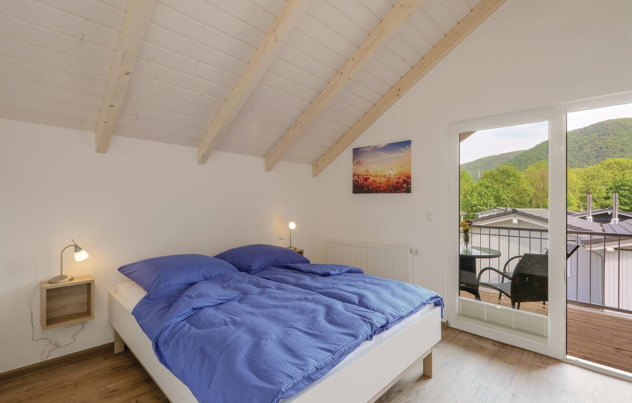 Une chambre à coucher comprenant un lit, deux lampes de chevet, un radiateur et une grande fenêtre donnant sur un balcon et de la verdure.