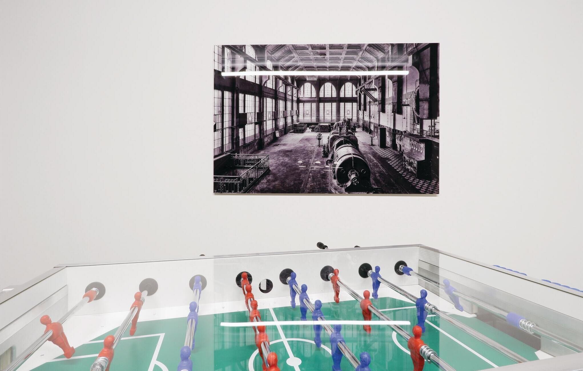 A room with a foosball table and a large black and white photograph of an industrial setting on the wall.