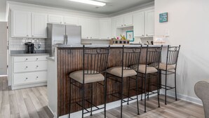 Une cuisine moderne avec des meubles blancs, un réfrigérateur en acier inoxydable et un îlot central en bois doté de tabourets de bar.