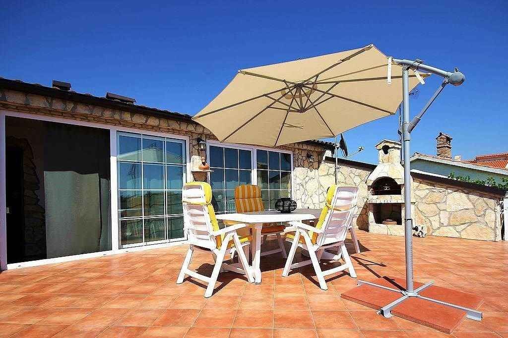 An outdoor patio with a table and chairs, a large umbrella, and a stone fireplace.