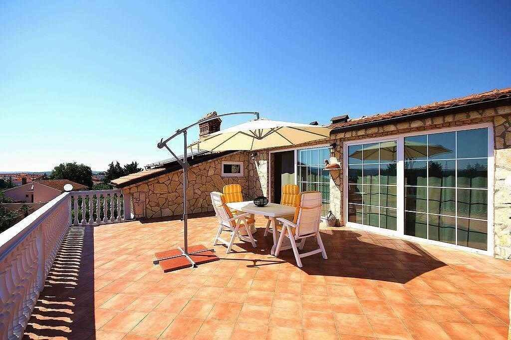 En tagterrasse med et bord, stole, en pergola og en stenvæg.
