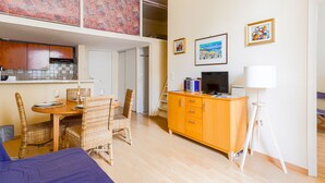 Un espace de vie compact comprenant un coin repas, une kitchenette et un téléviseur posé sur un meuble.