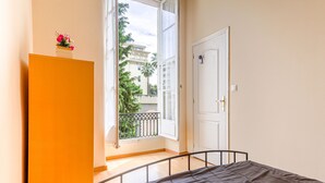 Une chambre à coucher comprenant un lit, une armoire et un balcon offrant une vue sur les immeubles et les arbres.