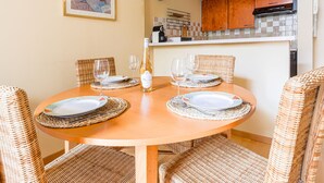 Un coin repas avec une table ronde en bois, des chaises en osier et une bouteille de vin.