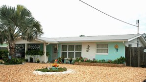 Ein Haus mit Veranda, einer Palme und einem Schotterweg.