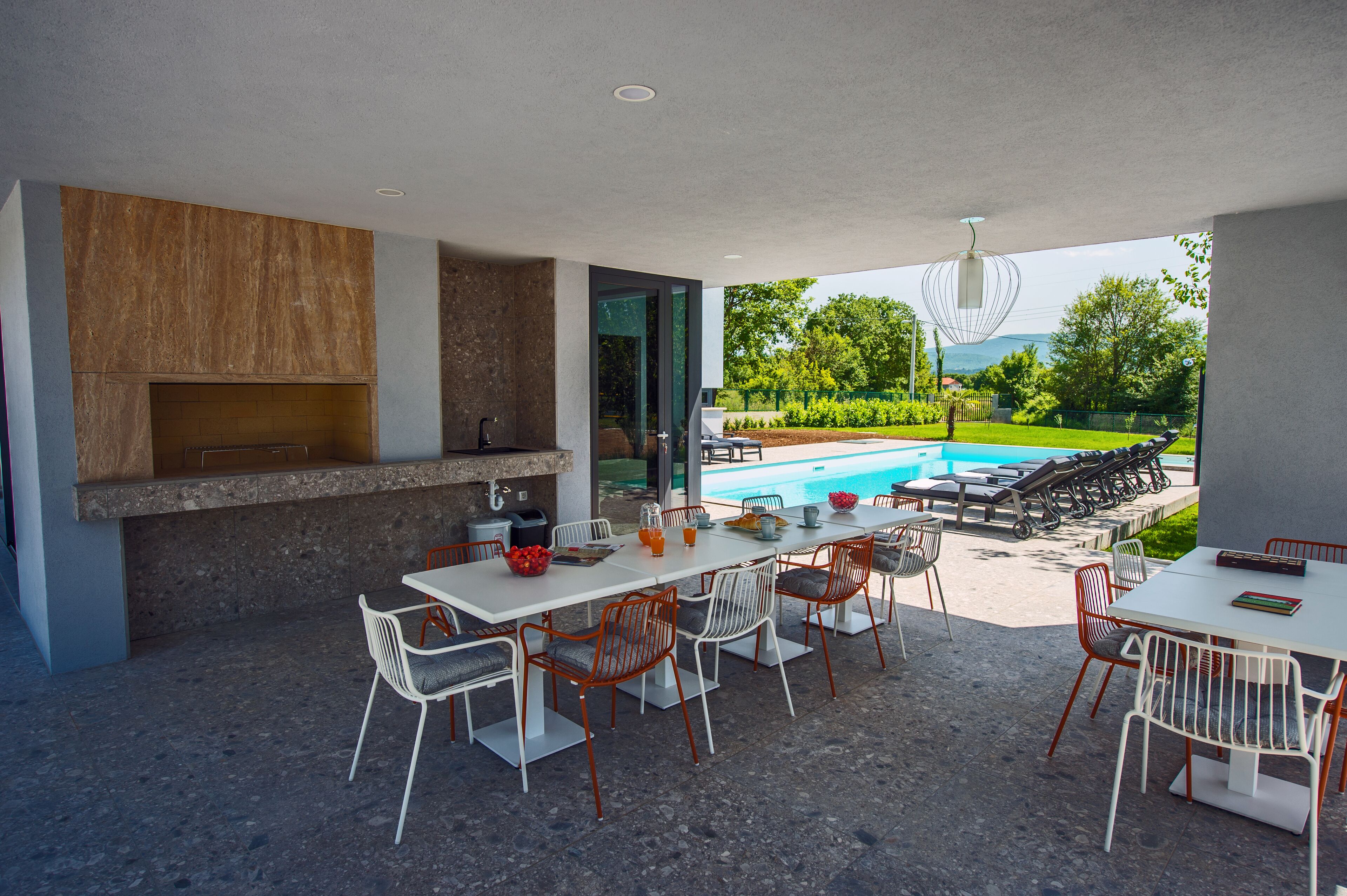 Un área de comedor al aire libre con vista a la piscina, cocina moderna y mobiliario exterior.