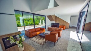 A modern living room with a sofa set, a coffee table, and a TV. There is a large window offering a view of greenery outside. - LUXURY 7 BEDROOM VILLA  WITH PRIVATE POOL,TENNIS COURT,GYM AND SPA (Donji Proložac)