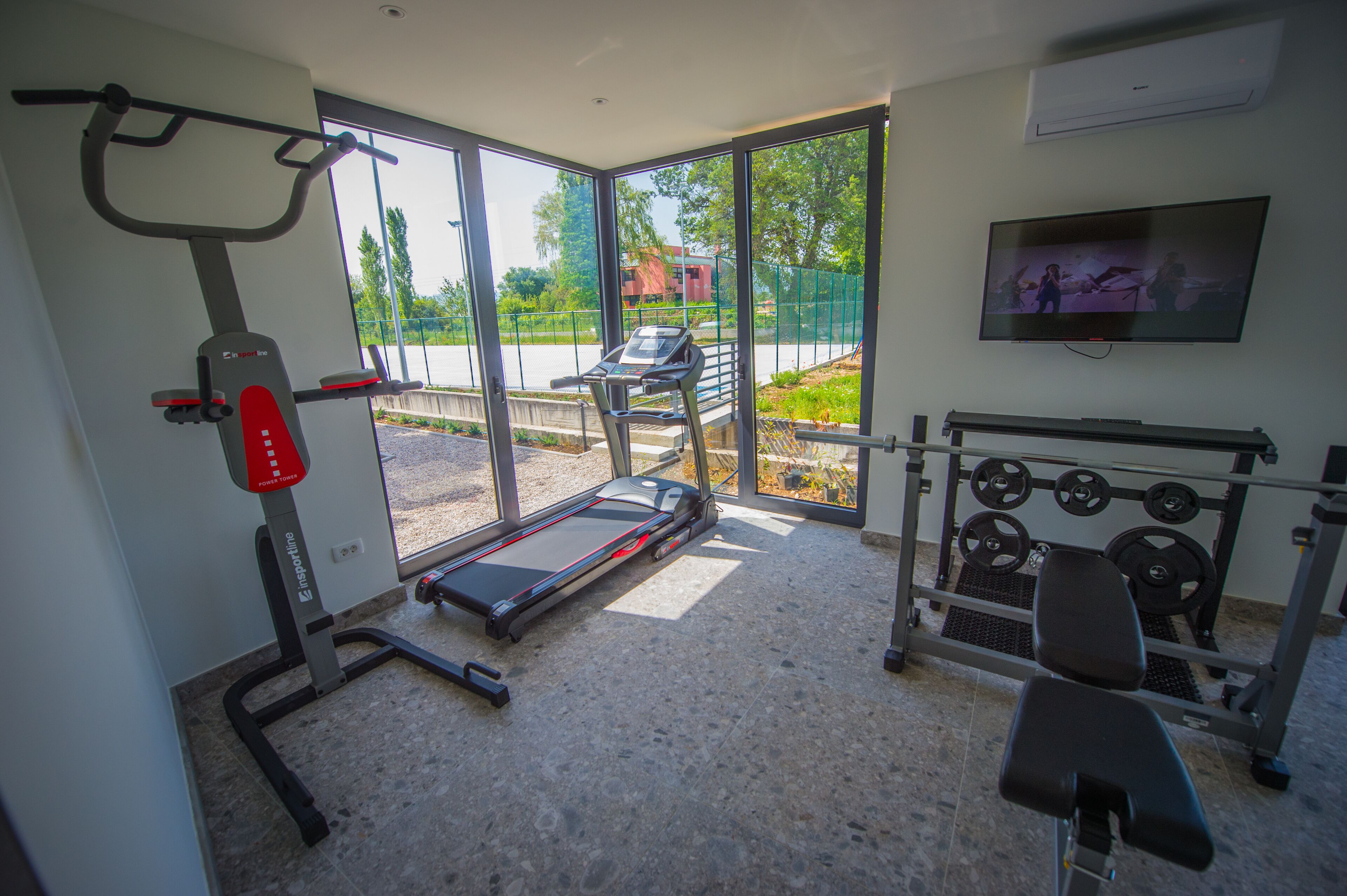 Un gimnasio con cinta de correr, banco de pesas y soporte para pesas.