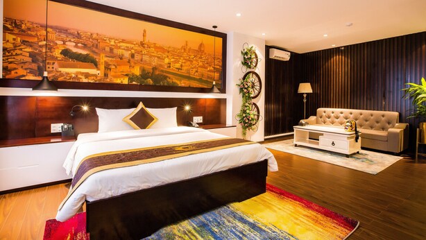 A modern hotel room with a large bed, a sofa, a coffee table, and a cityscape painting on the wall.