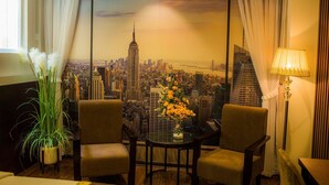 A room with a cityscape view, two chairs, a table with a vase of flowers, a lamp, and a potted plant.