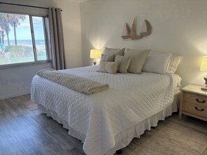 A bedroom with a large bed, a window with curtains, a bedside table with a lamp, and a wall-mounted decoration.