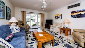A living room with a blue sofa, beige armchairs, a wooden coffee table, and a ceiling fan.