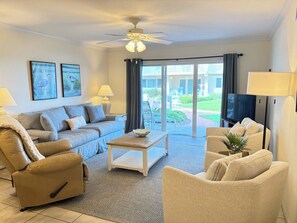 A living room with a sofa, armchair, coffee table, and a ceiling fan.