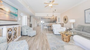 A spacious living room with a large painting, a ceiling fan, and a dining area in the background.