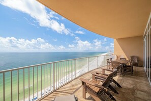 Un balcón con vista al océano y la playa, amueblado con sillas y mesas de madera.