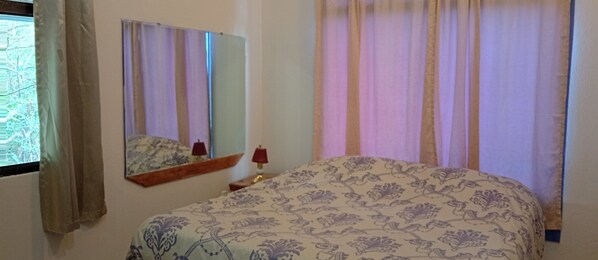 A bedroom with a bed, a nightstand, a lamp, a mirror, and curtains. - MONTEVERDE - Comfy, well-equipped  Cottage in woods with view! (Santa Elena)