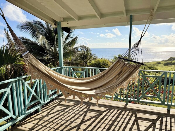 Eine Hängematte auf einem Balkon mit Blick auf das Meer und Palmen.