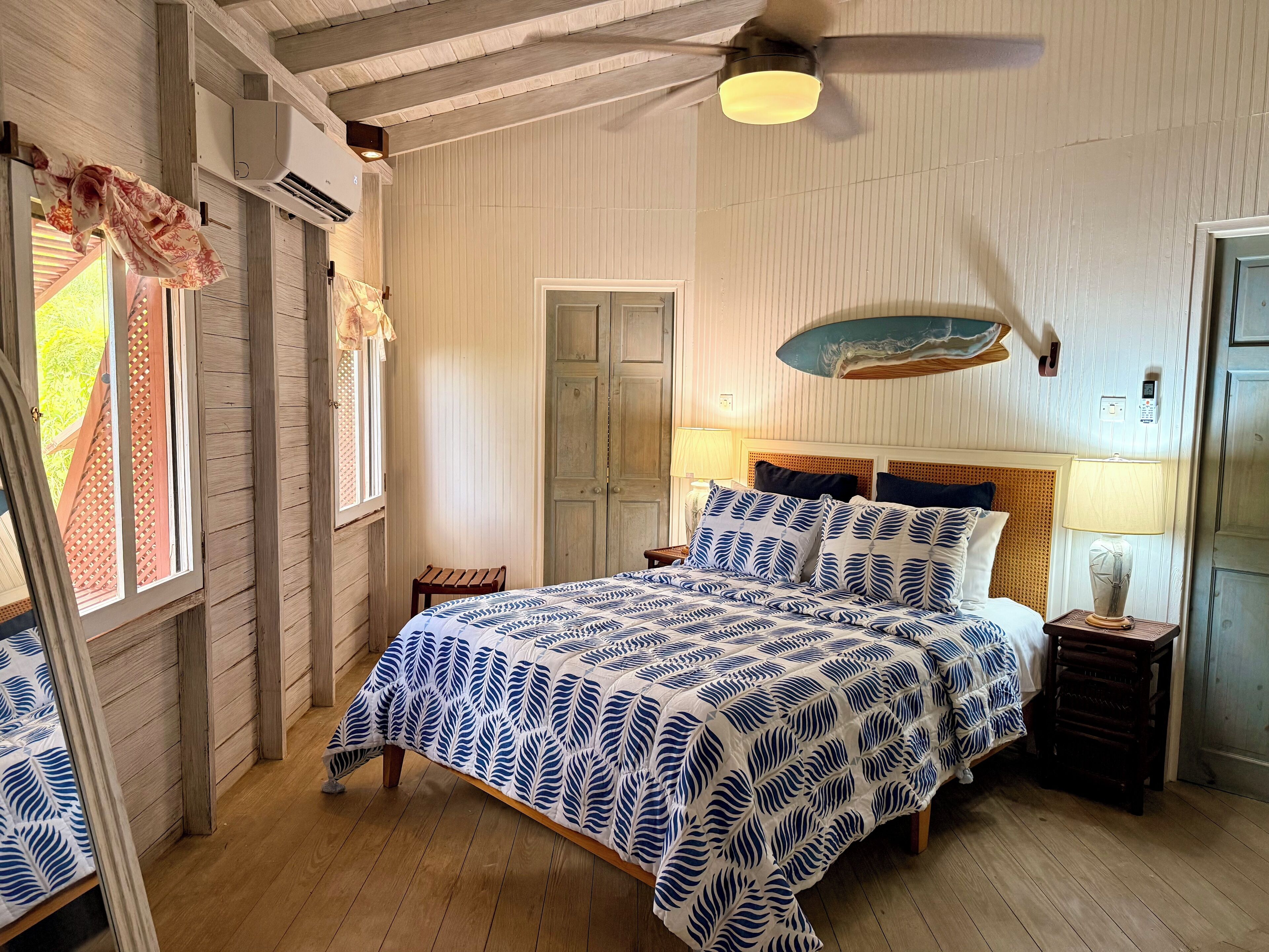 Une chambre à coucher avec un lit, un plancher en bois, un ventilateur de plafond et une fenêtre avec des rideaux.