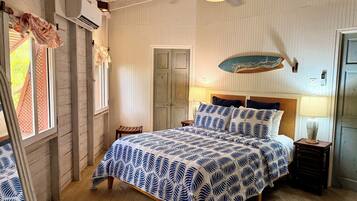 Une chambre à coucher avec un lit, un plancher en bois, un ventilateur de plafond et une fenêtre avec des rideaux.