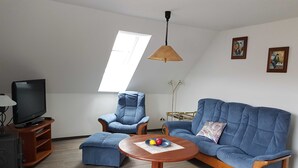Una sala de estar con un sofá, dos sillones, una mesita de centro, un televisor y un ventilador de techo.