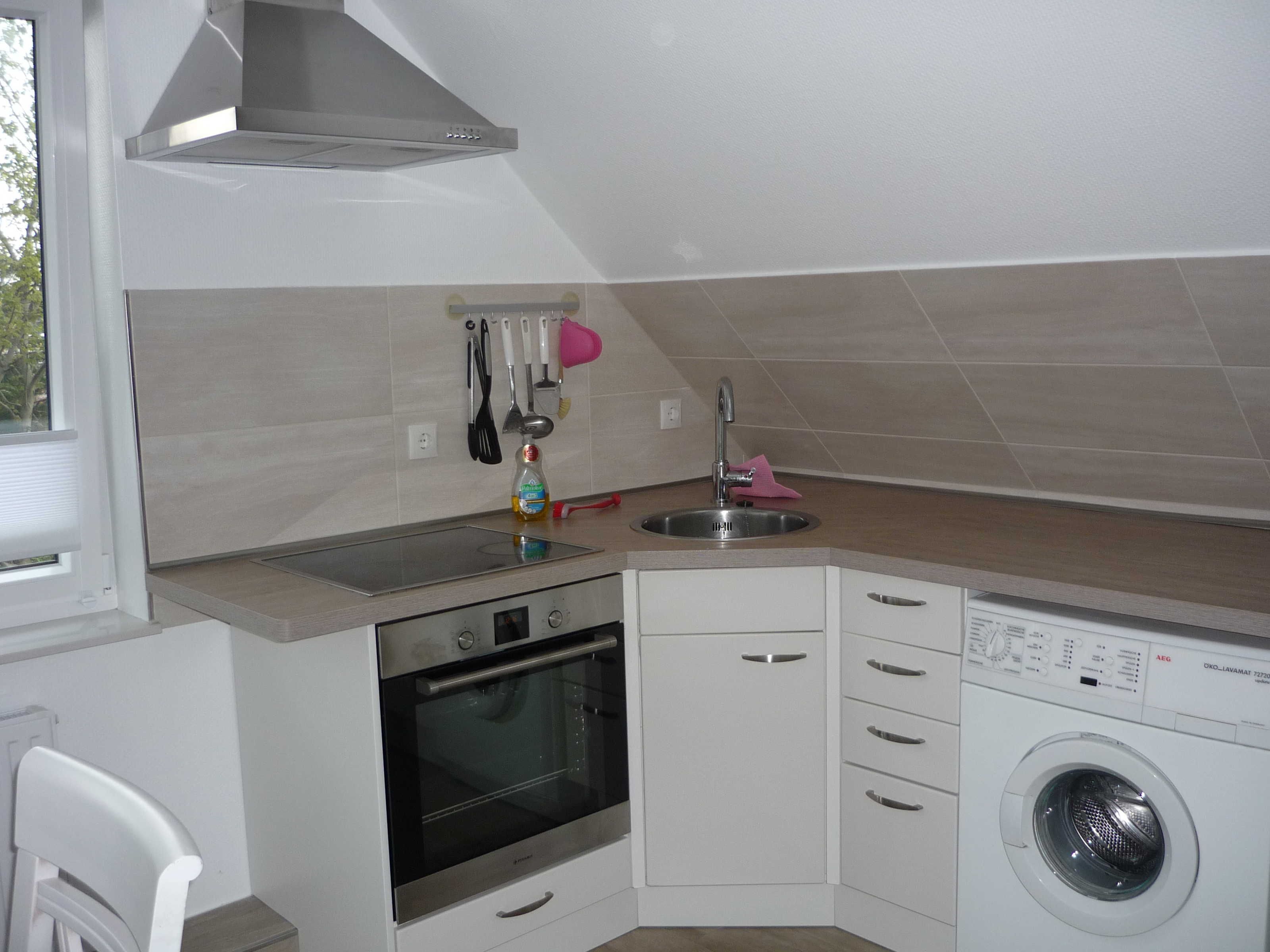 A compact kitchen with a built-in oven, a washing machine, and a sink.