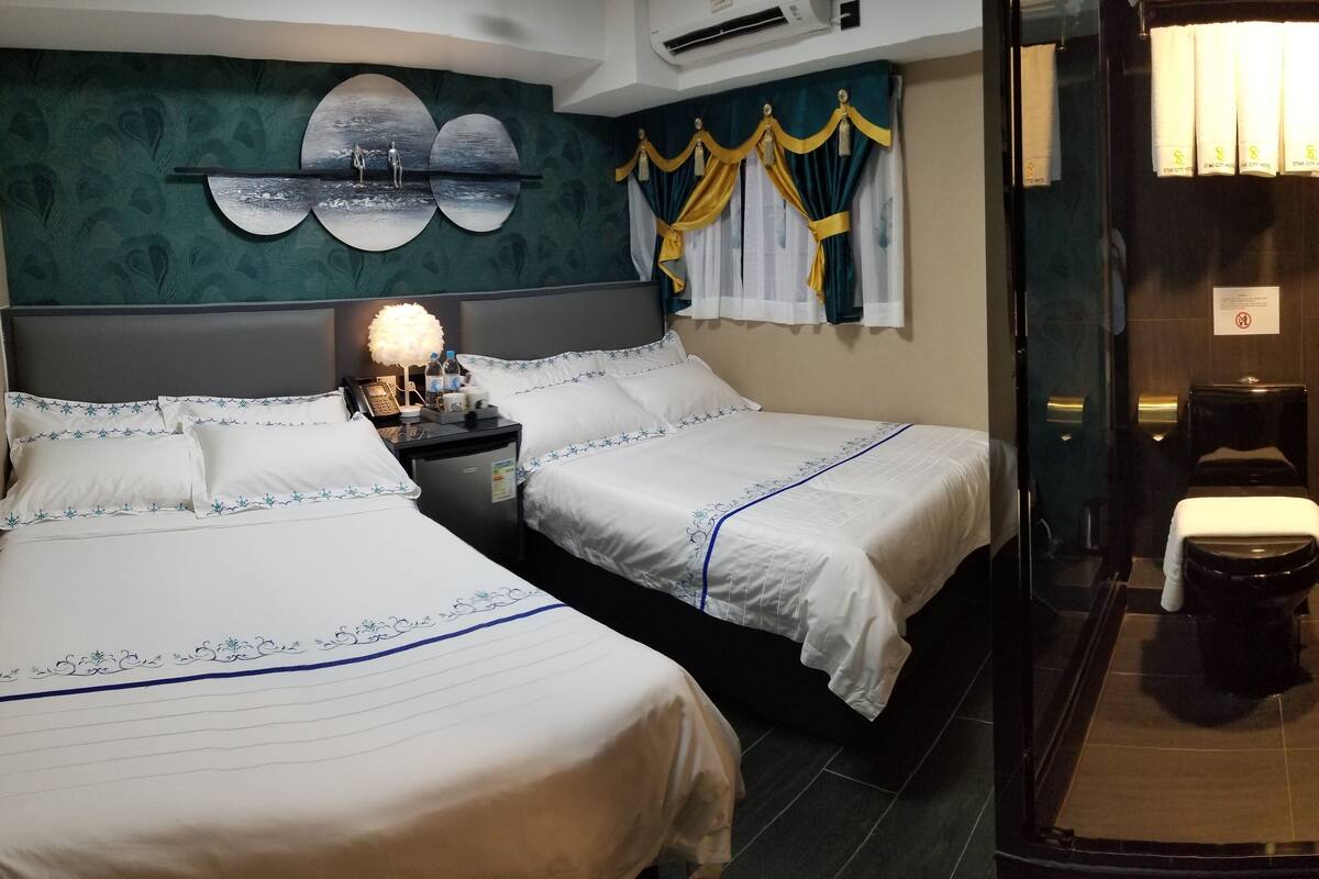 Une chambre d’hôtel avec deux lits, une table de chevet avec une lampe et une salle de bain avec des toilettes et une douche.