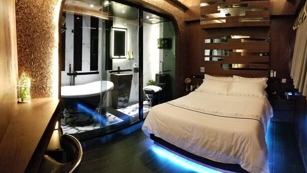 A modern bedroom with a large bed, a glass-enclosed bathroom, and a unique wall design.