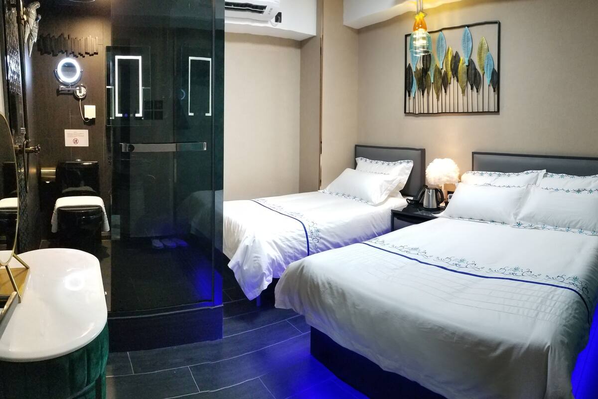 Une chambre d’hôtel avec deux lits, une salle de bain dotée d’une douche à parois de verre et un climatiseur fixé au mur.