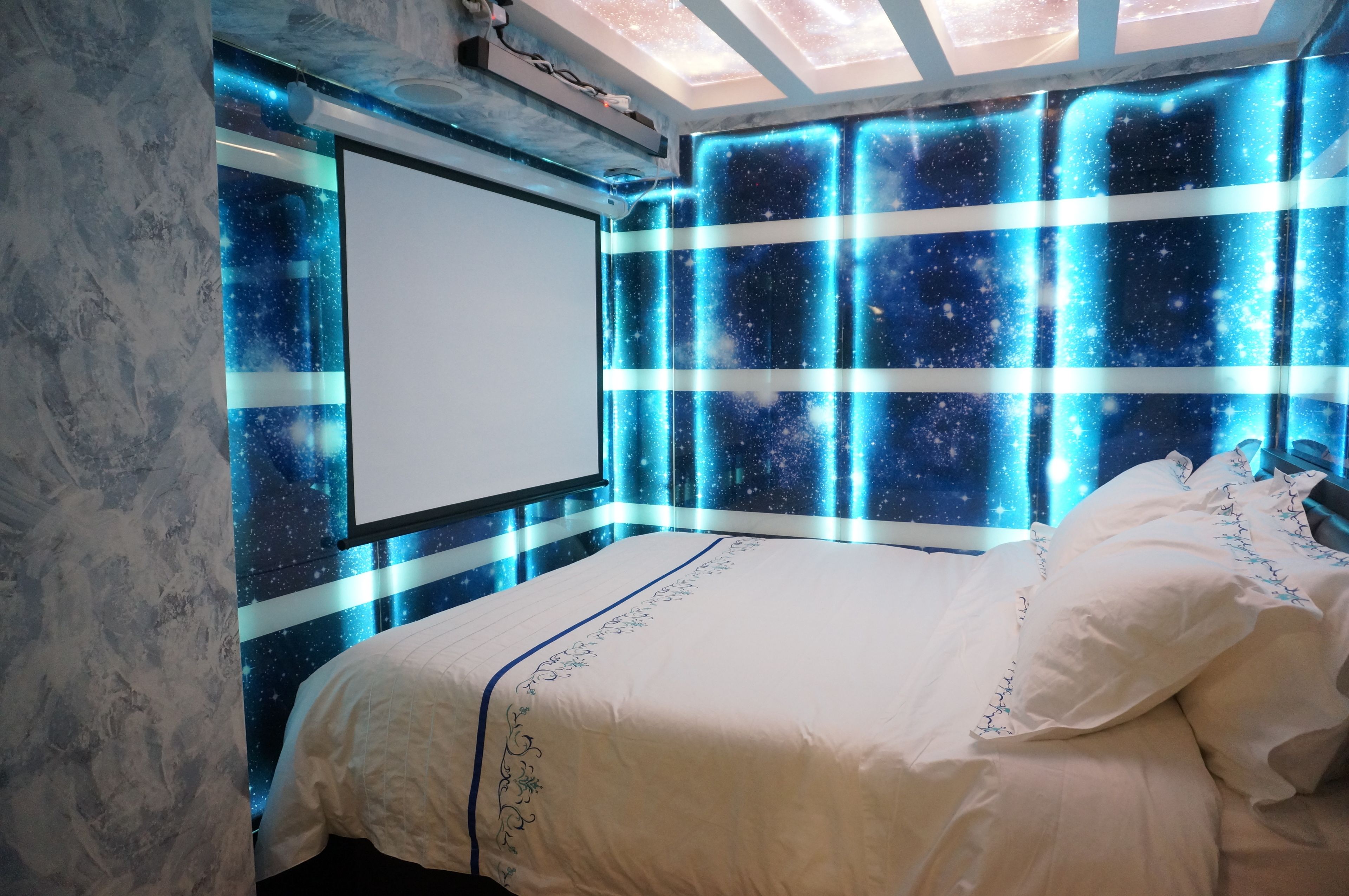 A bedroom with a bed, a projector screen, and a wall with a starry pattern.