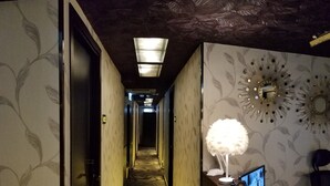 A hotel hallway with patterned wallpaper, a reception desk with a lamp, and a mirror.