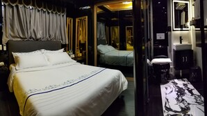 A hotel room with a large bed, a bathroom with a mirror, and a small table.