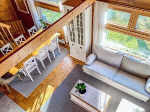 A loft-style room with a wooden staircase, a sofa, a dining table with chairs, and a view of greenery outside. - Villa rauha by Interhome (Soini)