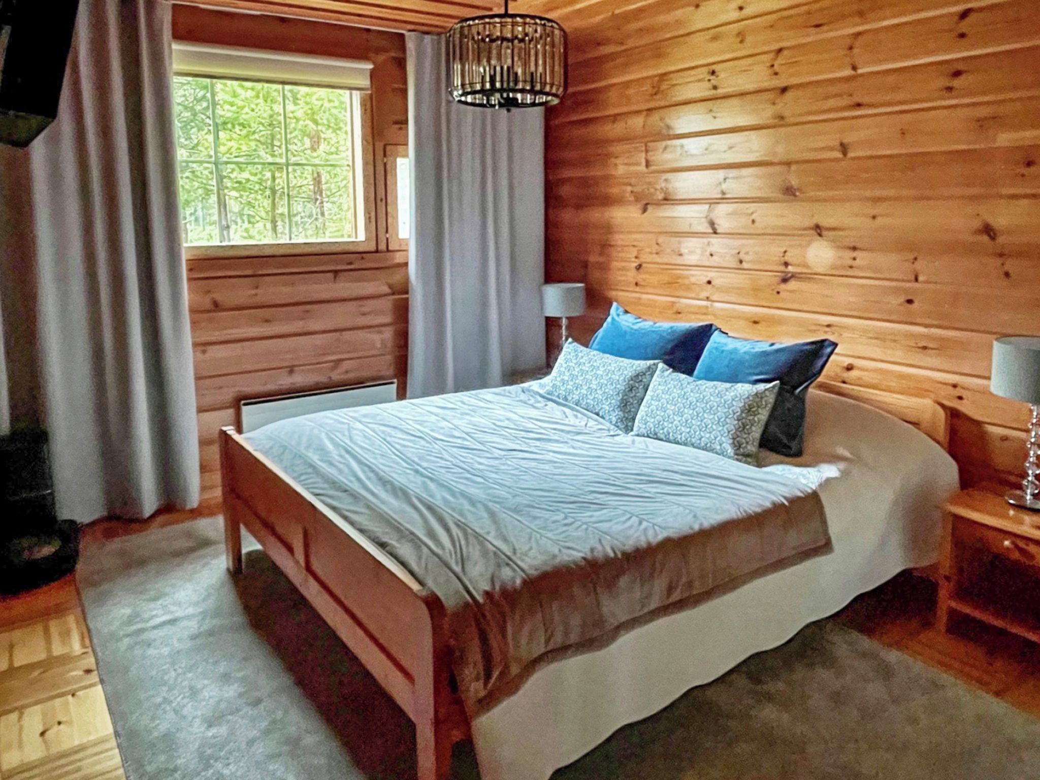 Een kamer met houten lambrisering, een bed, een raam met gordijnen en een hanglamp.
