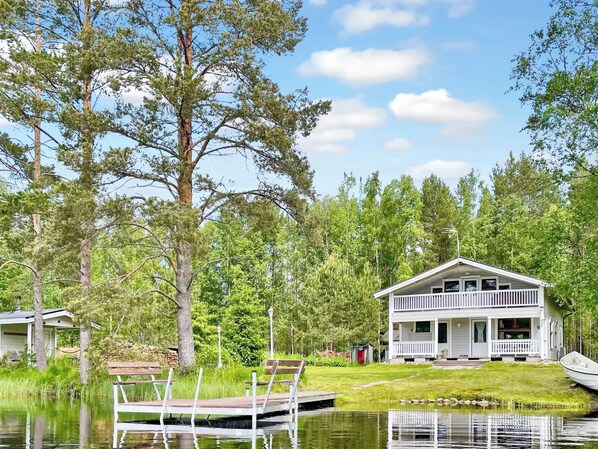 A lakeside cabin with a dock, surrounded by trees and a clear sky.