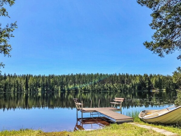 A calm lake with a dock and a boat, surrounded by dense forest. - Villa rauha by Interhome (Soini)