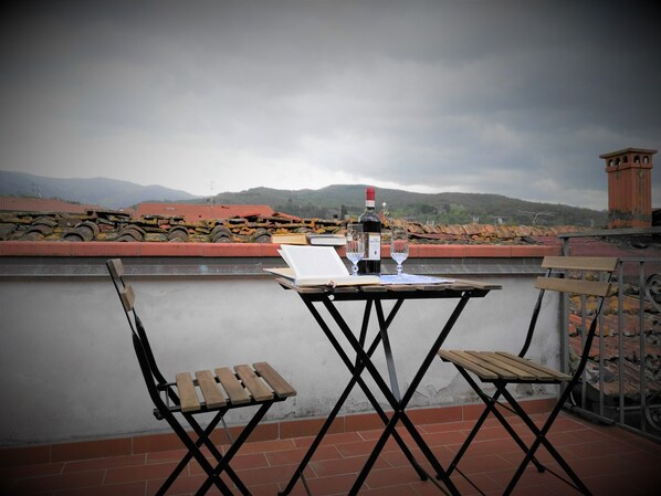 A terrace with a table set for two, featuring a bottle of wine and glasses, and two wooden chairs.