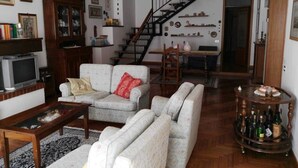 Ein Wohnzimmer mit einer Sofagarnitur, einem Fernseher, einem Holzschrank, einer Treppe und einem Essbereich.
