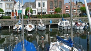 A marina with several boats docked, a stone wall, and buildings with traditional architecture in the background.
